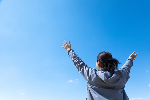 青空に向かって両手を広げる人の後ろ姿